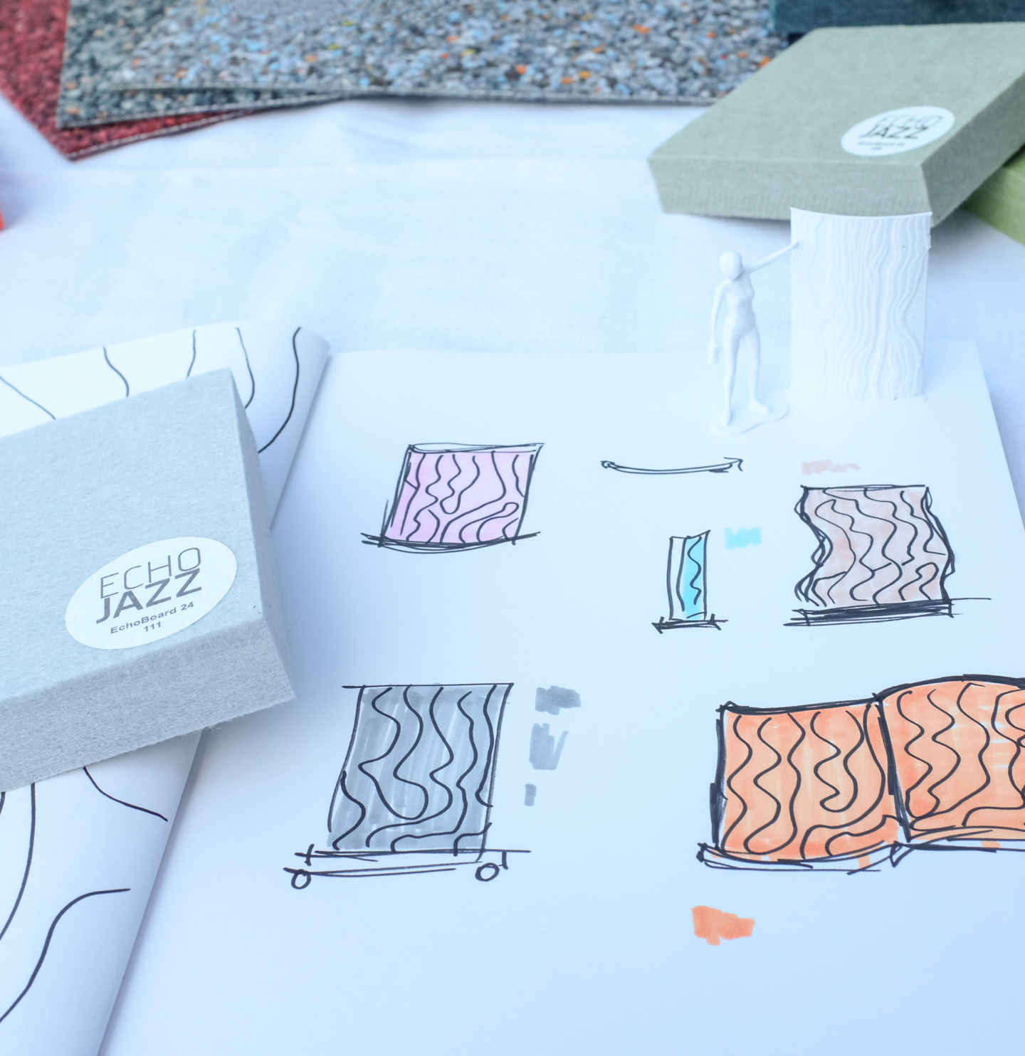 Prozesssaufnahme, farbige Skizzen des Raumtrenners mit Akustikmaterialmuster und 3D-gedruckten Modellfiguren.